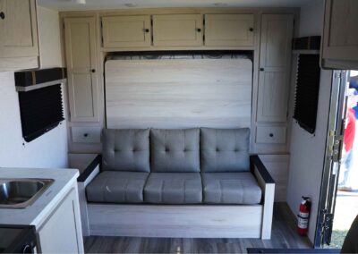 View of a Murphy bed, with the bed folded up into the wall and a couch in its place. You can also see the door and part of the kitchen.