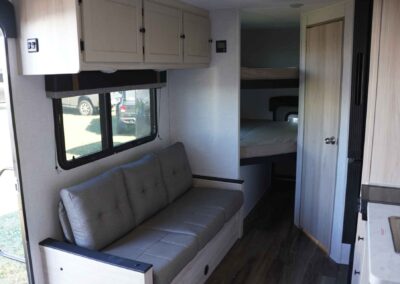 The main area of the 21' comfort line camper, with a couch on one wall, and the kitchenette on the other. You can also see two bunks/sleeping spaces.